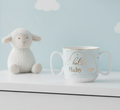 White mug with 'Hello Baby Foo' text next to a white lamb toy on a light blue background