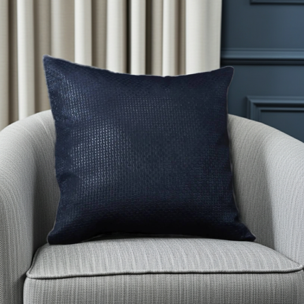 Navy blue textured cushion on a gray armchair with beige curtains in the background