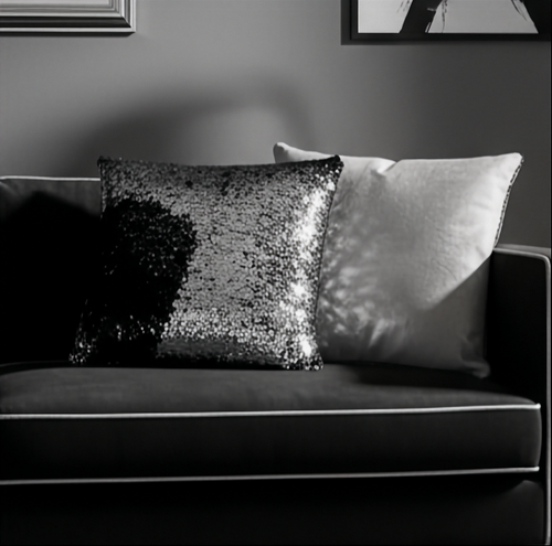 Gray sofa with a black and silver sequin cushion and a plain pillow against a gray wall.