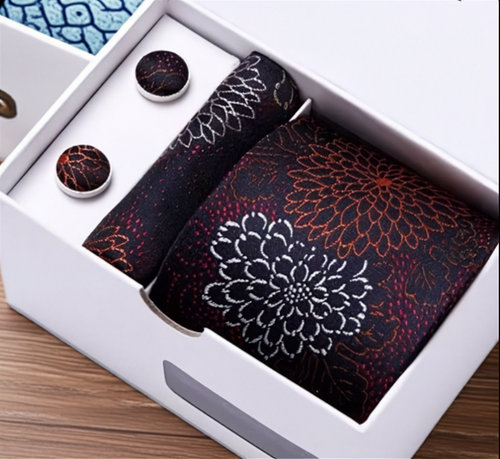 Floral-patterned tie and cufflinks set in a white box on a wooden surface