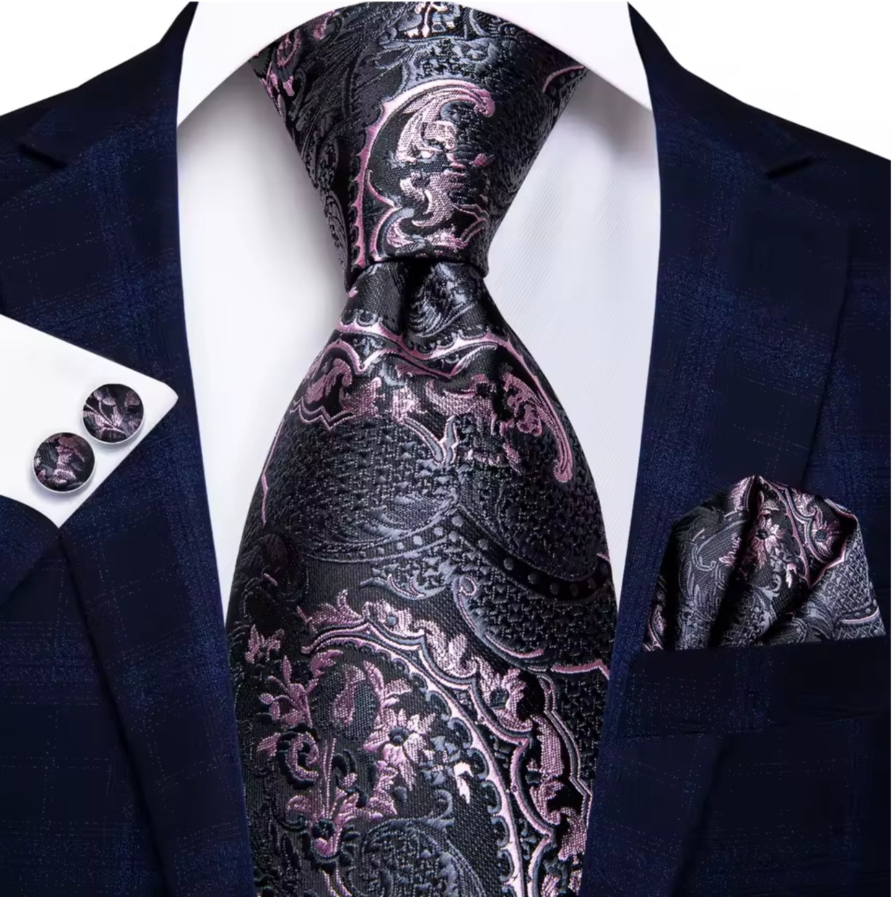 Navy suit with a black and pink paisley tie, pocket square, and cufflinks on a white background