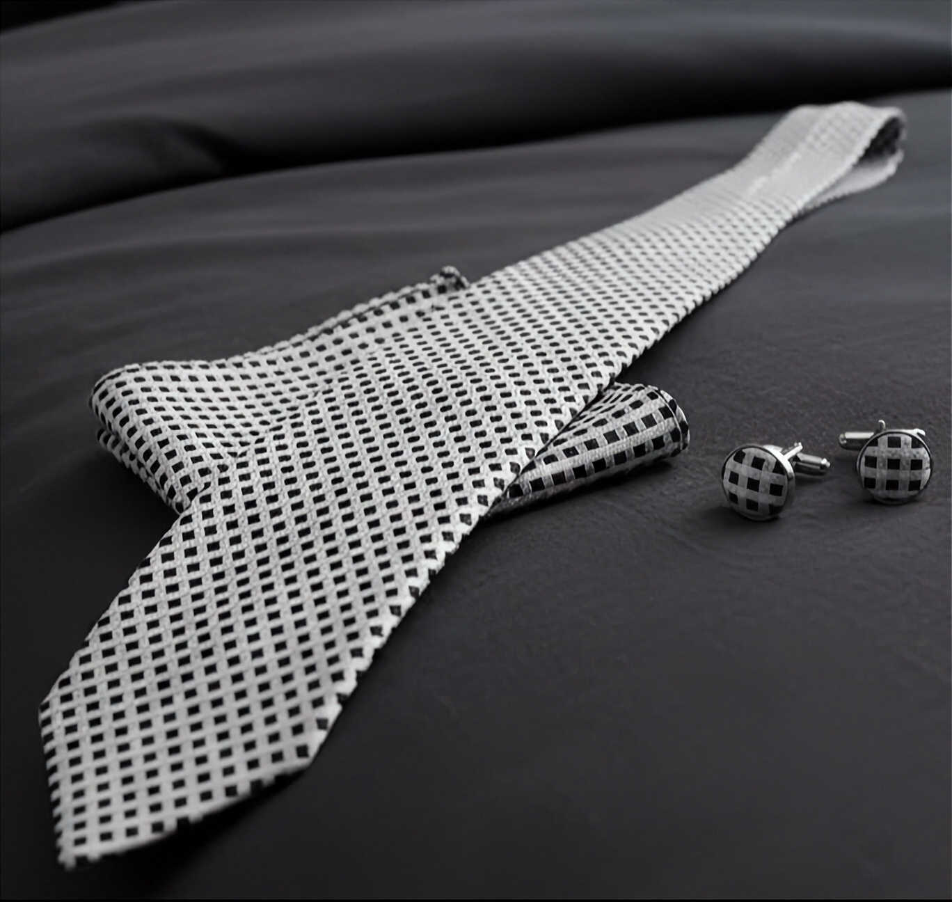 Black and white patterned bow tie and cufflinks on a dark fabric background