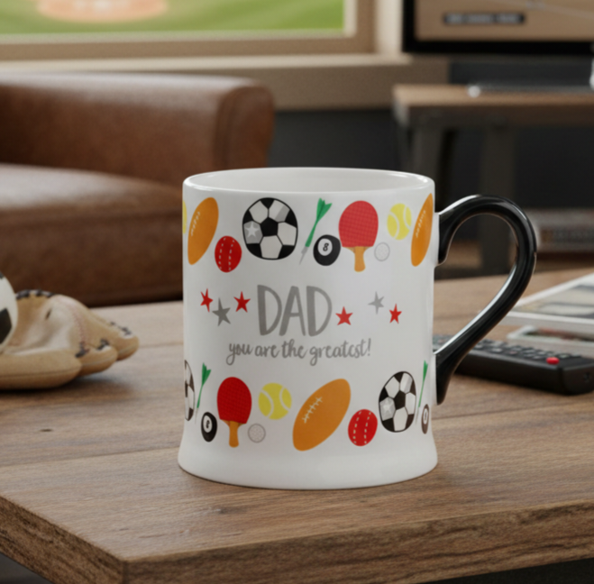 White mug with sports-themed design and 'DAD you are the greatest!' text on a wooden table.