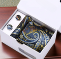 Dark green paisley pocket square with gold accents and matching cufflinks in a white box on a wooden surface.