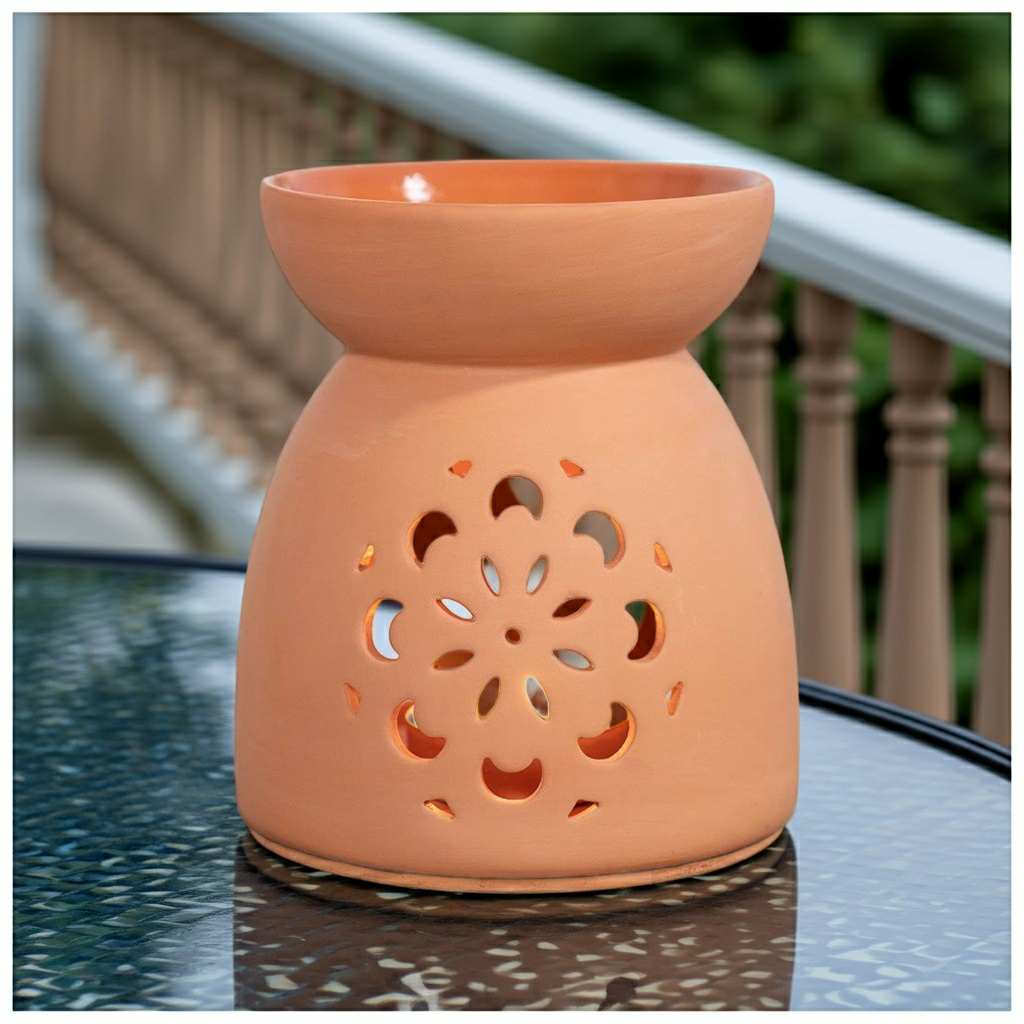Terracotta-colored ceramic oil burner on a reflective surface with blurred background