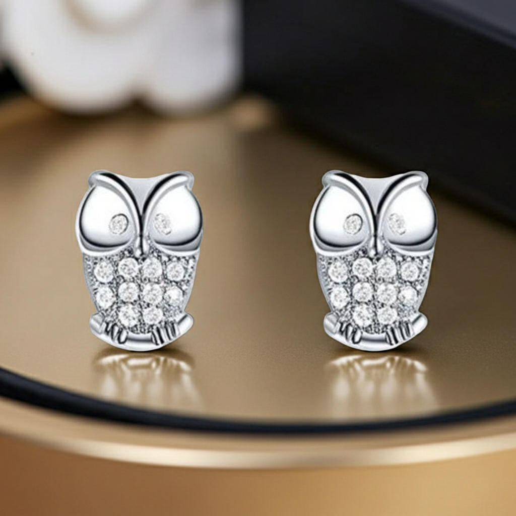 Silver owl earrings with clear stones on a reflective surface
