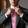 Man adjusting a pink tie in a gray suit against a neutral background