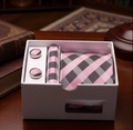 Pink and gray checkered tie set with cufflinks in a box on a wooden surface.