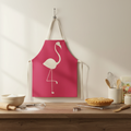 Pink apron with a flamingo design hanging on a hook above a kitchen counter.