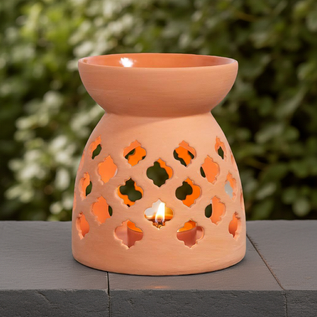 Terracotta oil burner with cut-out designs on a stone surface with a blurred green background