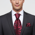 Man wearing a black suit with a red paisley tie and pocket square on a light gray background