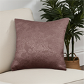 Decorative dusky pink cushion with floral pattern on a beige sofa next to a plant
