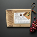 Wooden cutting board with brand label on a dark surface, accompanied by grapes.