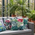 Decorative outdoor cushions with tropical leaf patterns on a patio with plants in the background.